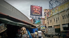 Billboards. Signages block the skyline in populated areas in Manila such as this one. The women at the center carry plastic bags of goods as they walk past a store. Lines of store, such as the souvenir store on the left, can be found underneath elevated roads.