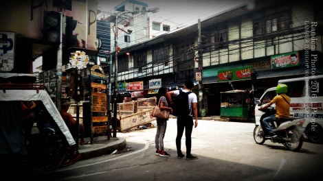 A young couple under a building's shadow. A young couple stops before a crossing.